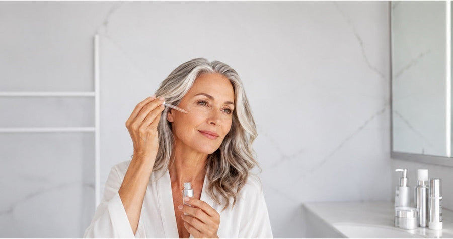 Woman applying an anti-aging peptide facial serum with a dropper in a bathroom