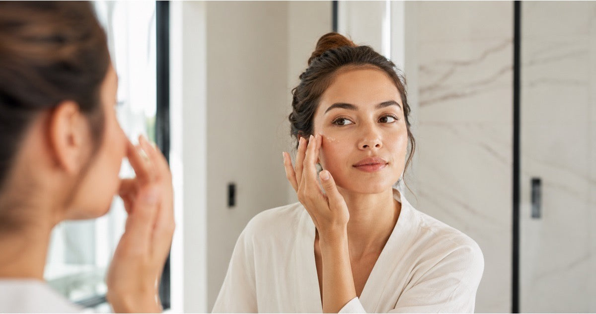 Woman applying peptide skincare in front of a bathroom mirror